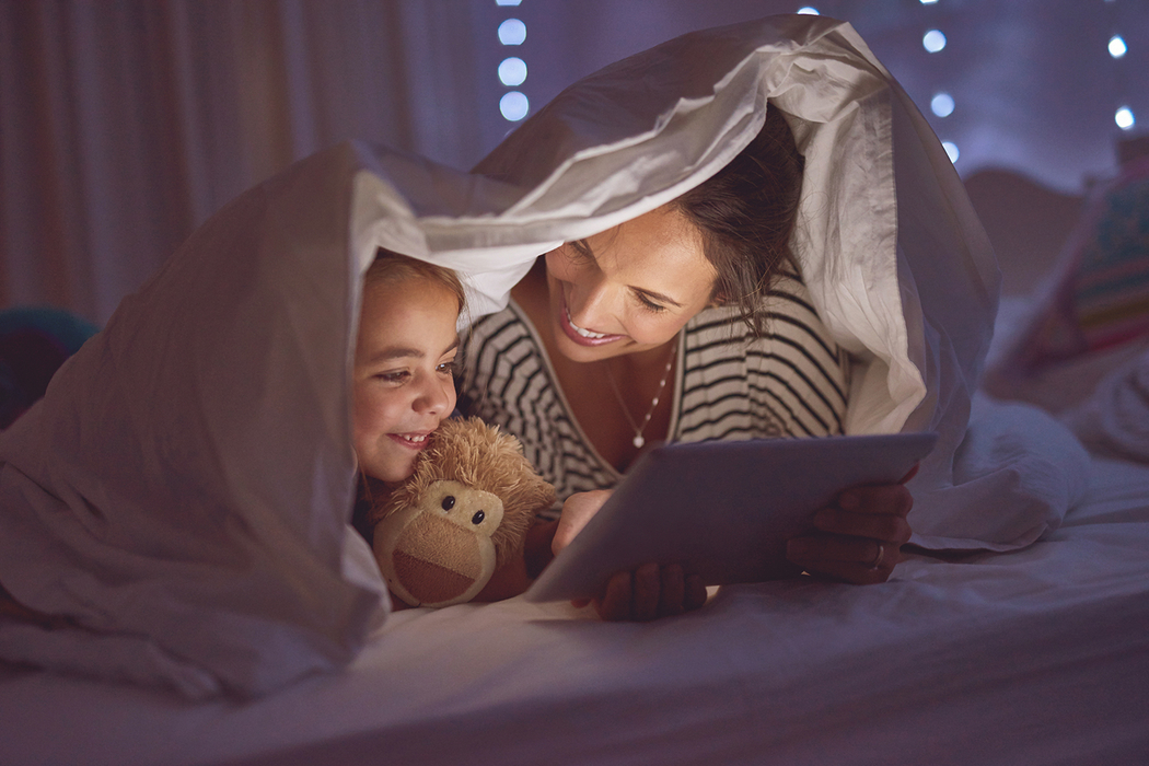 Mutter und Kind schauen auf dem Tablet unter der Bettdecke