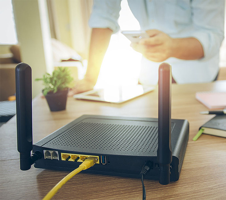 Ein Mann steht vor einem Router und hält ein Smartphone in der Hand.