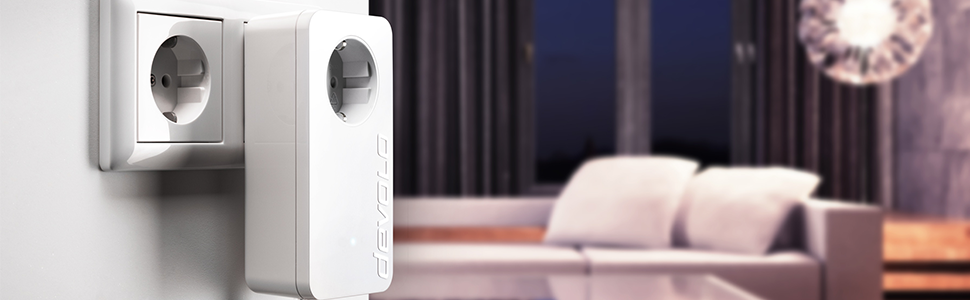 Ein devolo Powerline-Adapter in einer Steckdose an der Wand angeschlossen. In Hintergrund ein Couch mit zwei große Kissen drauf.