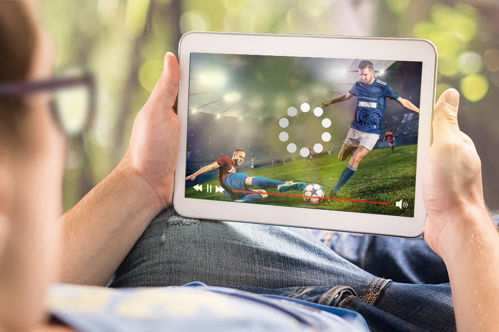 Ein Mann schaut Fußball auf einem Tablet. Der Stream stockt jedoch und es ist nur ein Standbild mit Ladekreis zu sehen.