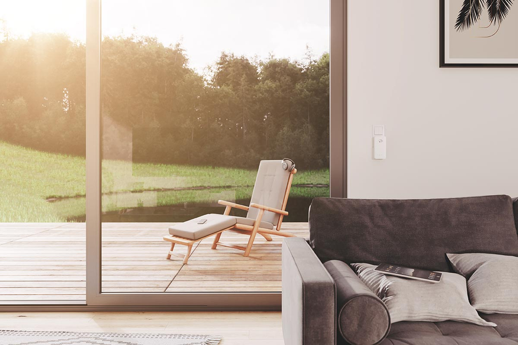 Couch im Wohnzimmer. In einer Steckdose neben der Gartentür steckt an der Wand ein devolo Powerline Adapter dLAN 1200 WiFi ac.