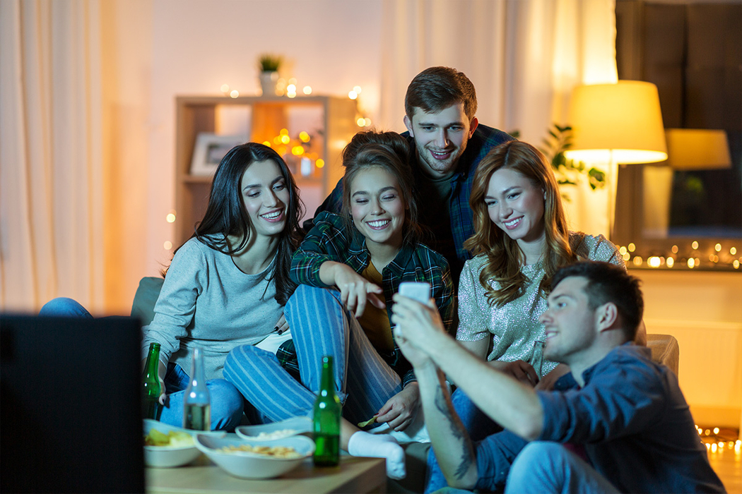Familie sitzt auf dem Couch im Wohnzimmer und schaut Fern. Das kleine Mädchen hält ein Schüssel aus Glas in den Händen.