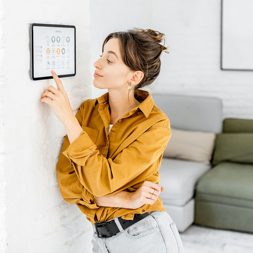 Eine Frau lehnt an ihrer Wohnzimmerwand und bedient ein Smart-Gerät.