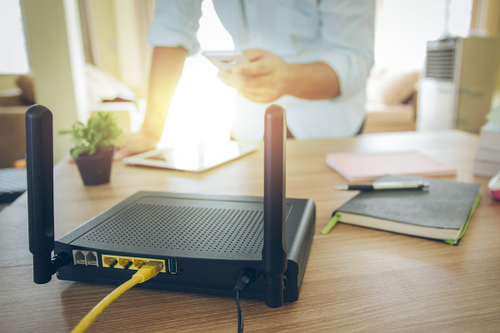 Router auf dem Schreibtisch und Mann steht neben an mit einem Smartphone in der Hand