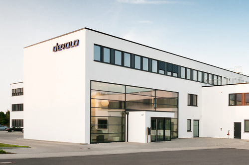 The devolo building in Aachen. A large white building with many windows and the devolo logo in black.